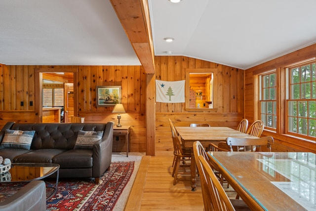 dining space with light hardwood / wood-style floors, lofted ceiling with beams, and wooden walls