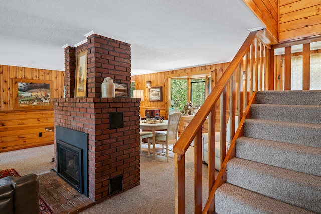 stairway with wood walls, carpet, brick wall, a textured ceiling, and a fireplace