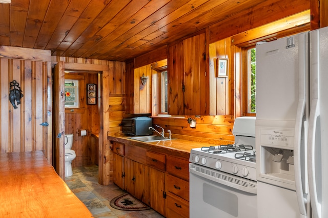 kitchen featuring sink, white appliances, wooden walls, light tile patterned floors, and wood ceiling