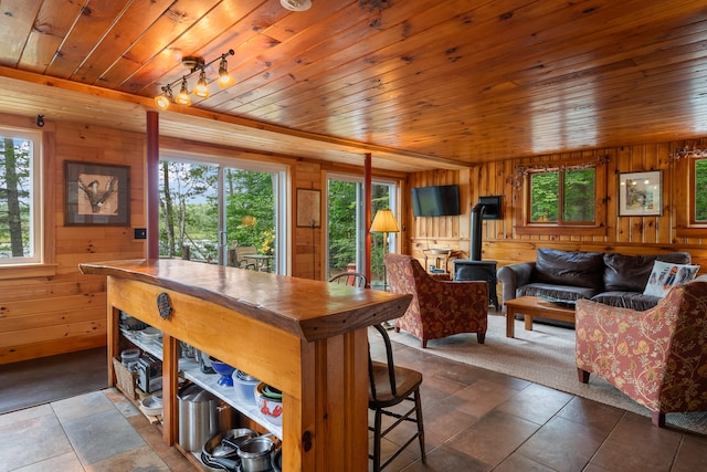 dining area with dark tile patterned flooring, wood ceiling, a wood stove, and wooden walls