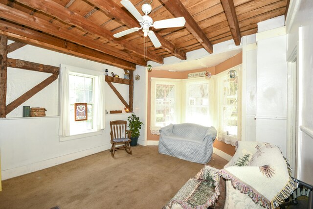 living area with ceiling fan, beamed ceiling, wood ceiling, and carpet