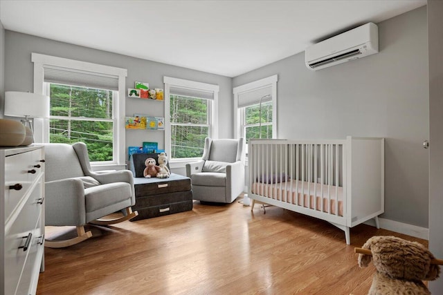 bedroom featuring a crib, light wood-type flooring, multiple windows, and a wall mounted AC