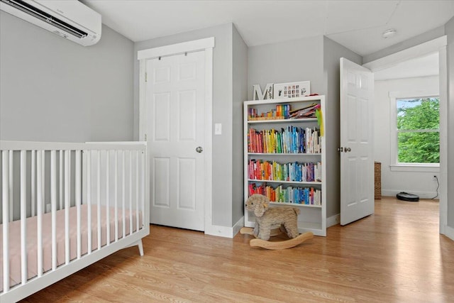 bedroom featuring light wood-type flooring, a crib, and an AC wall unit