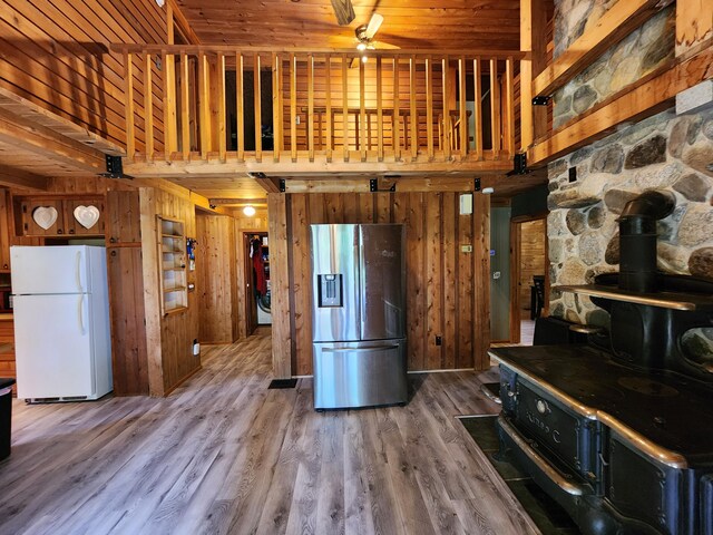 kitchen with hardwood / wood-style flooring, stainless steel refrigerator with ice dispenser, wood walls, white fridge, and a wood stove