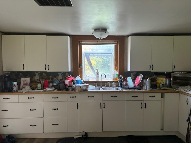 kitchen with tasteful backsplash, visible vents, white cabinets, light countertops, and a sink