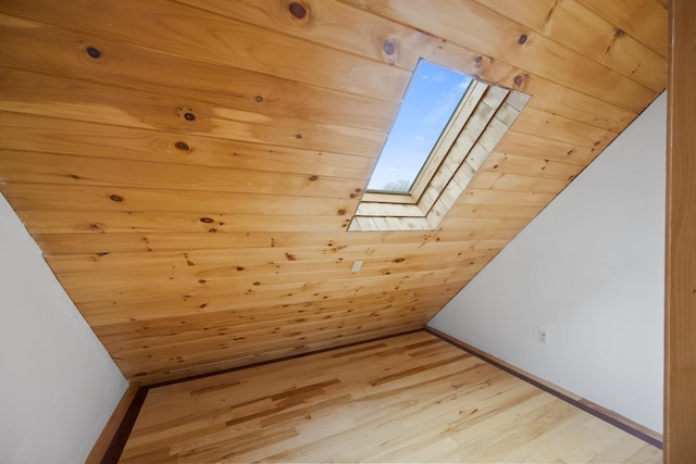 additional living space with wooden walls, light wood-type flooring, and lofted ceiling with skylight