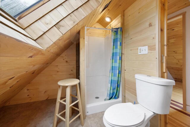 bathroom with curtained shower, vaulted ceiling with skylight, wooden walls, and toilet