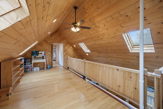 bonus room with light wood-type flooring, ceiling fan, wood ceiling, wood walls, and vaulted ceiling with skylight