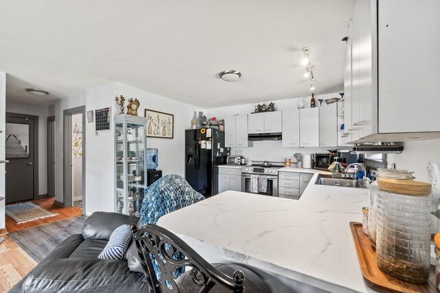 kitchen featuring sink, black fridge with ice dispenser, kitchen peninsula, stainless steel range oven, and hardwood / wood-style flooring