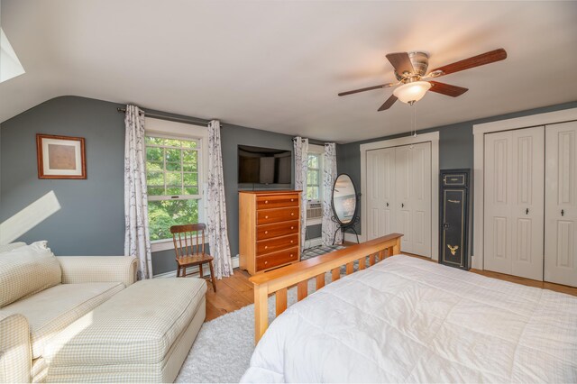 bedroom with lofted ceiling, ceiling fan, light hardwood / wood-style floors, and multiple closets