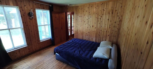 bedroom featuring multiple windows, wooden walls, and hardwood / wood-style floors