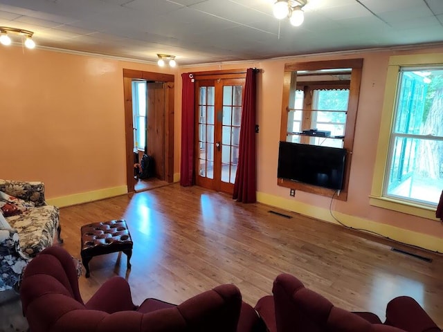 living room featuring light hardwood / wood-style floors, a healthy amount of sunlight, ornamental molding, and french doors