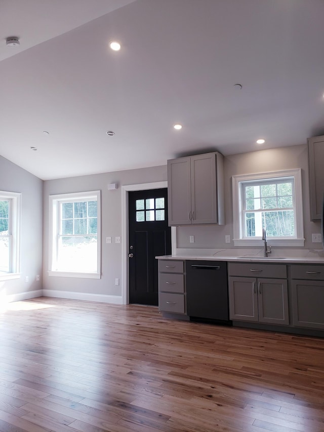 kitchen with black dishwasher, sink, light hardwood / wood-style floors, vaulted ceiling, and gray cabinetry