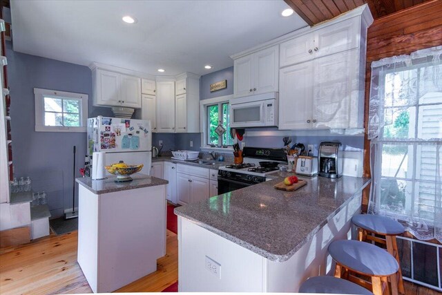 kitchen featuring white cabinets, light hardwood / wood-style floors, a breakfast bar area, a center island, and white appliances