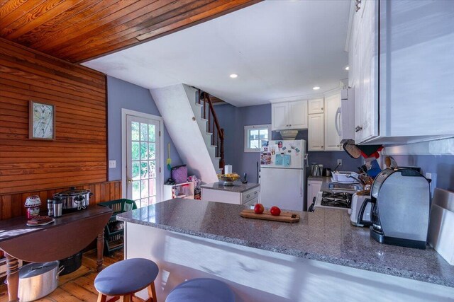 kitchen with white cabinetry, wooden walls, kitchen peninsula, white appliances, and hardwood / wood-style flooring