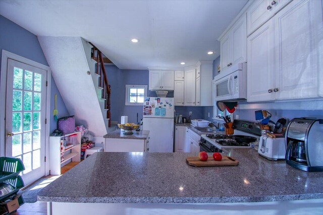 kitchen with dark stone counters, white cabinetry, sink, kitchen peninsula, and white appliances