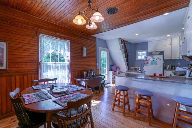 dining room featuring wood walls, a wealth of natural light, wooden ceiling, and light hardwood / wood-style flooring