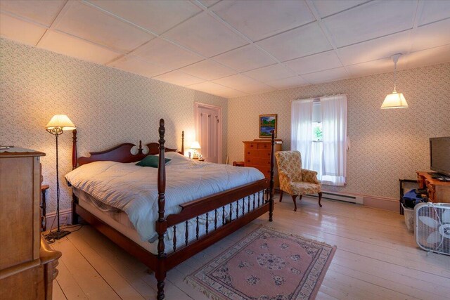 bedroom featuring a paneled ceiling, baseboard heating, and light wood-type flooring