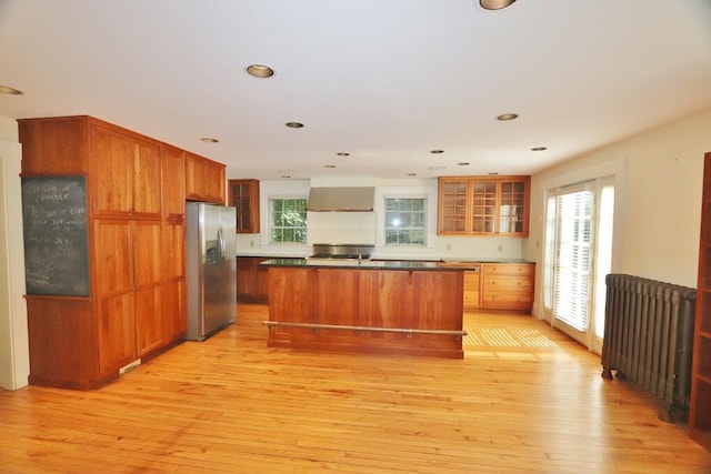 kitchen featuring stainless steel appliances, light hardwood / wood-style floors, a center island, and wall chimney range hood