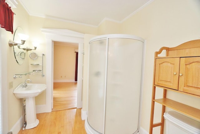 bathroom with hardwood / wood-style floors, ornamental molding, toilet, sink, and an enclosed shower