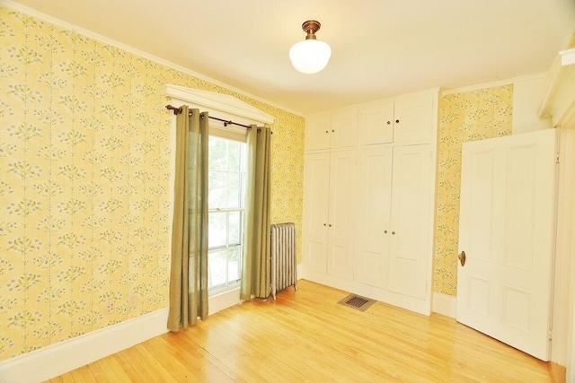 empty room featuring light wood-type flooring, crown molding, and radiator heating unit