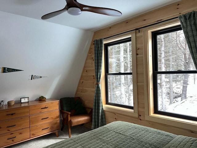 carpeted bedroom featuring ceiling fan and wood walls