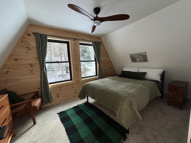 carpeted bedroom with ceiling fan, wooden walls, and vaulted ceiling