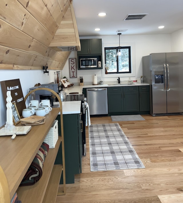 kitchen featuring appliances with stainless steel finishes, light hardwood / wood-style flooring, hanging light fixtures, and sink