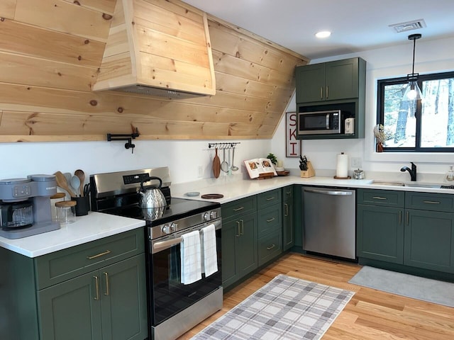 kitchen with green cabinets, sink, light wood-type flooring, decorative light fixtures, and stainless steel appliances