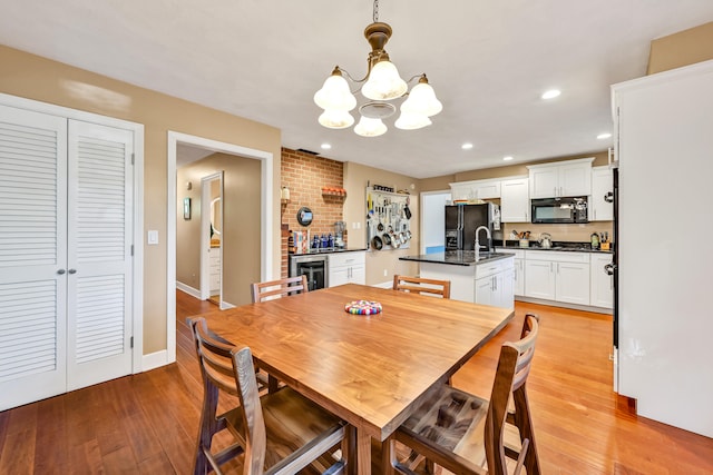 dining space featuring beverage cooler, sink, a notable chandelier, and light hardwood / wood-style flooring