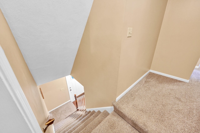 stairway with a textured ceiling, lofted ceiling, and carpet