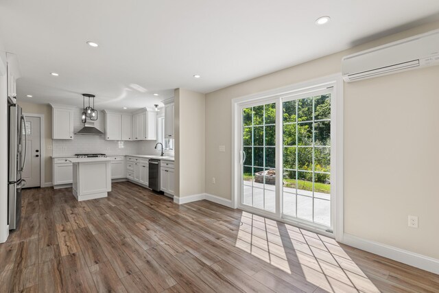 kitchen featuring a wall mounted AC, appliances with stainless steel finishes, light wood-type flooring, and hanging light fixtures