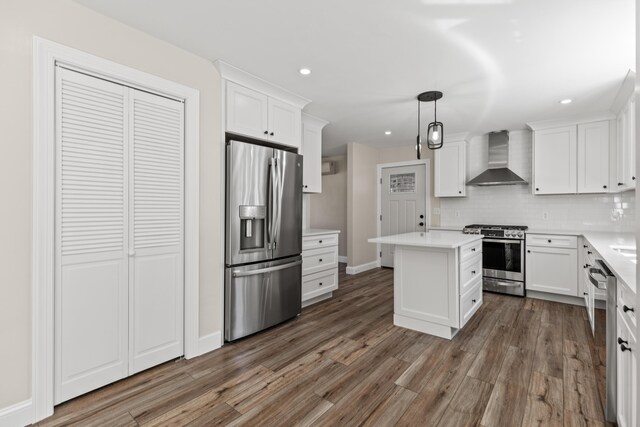 kitchen with hanging light fixtures, backsplash, stainless steel appliances, dark hardwood / wood-style floors, and wall chimney range hood