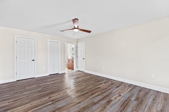 unfurnished bedroom featuring ceiling fan, wood-type flooring, and multiple closets