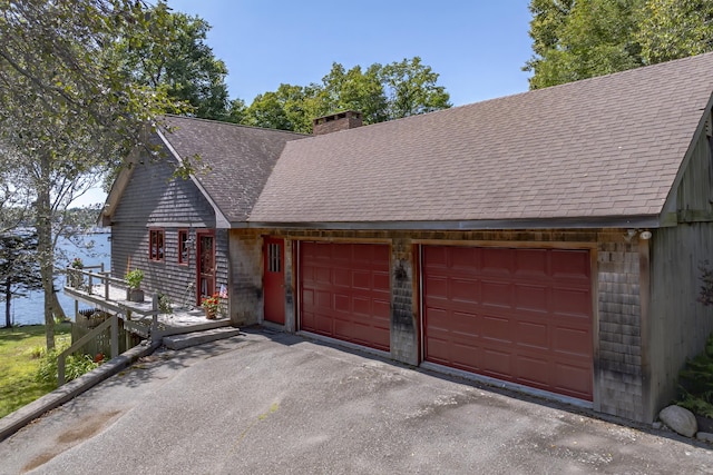 chalet / cabin featuring a chimney, a shingled roof, a water view, a garage, and driveway