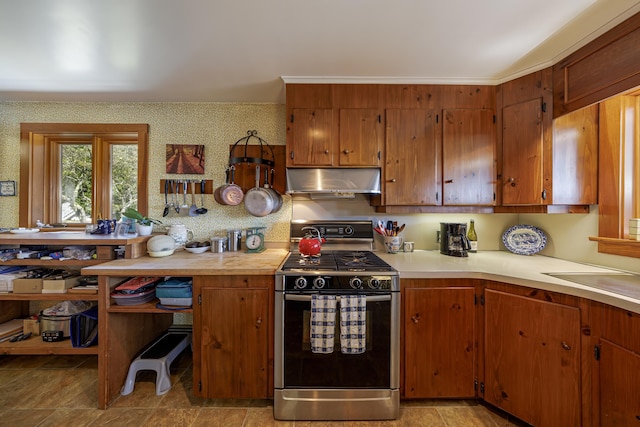 kitchen featuring under cabinet range hood, a sink, light countertops, brown cabinetry, and gas range