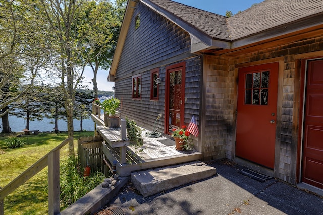 entrance to property featuring a water view and roof with shingles