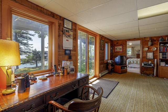 office area with carpet floors, a baseboard radiator, wooden walls, and a drop ceiling