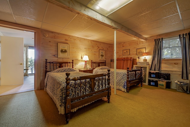 carpeted bedroom with a paneled ceiling and wooden walls