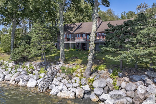 rear view of property featuring a chimney, a deck with water view, and a yard