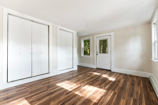 unfurnished bedroom with a baseboard radiator, dark wood-type flooring, and multiple closets