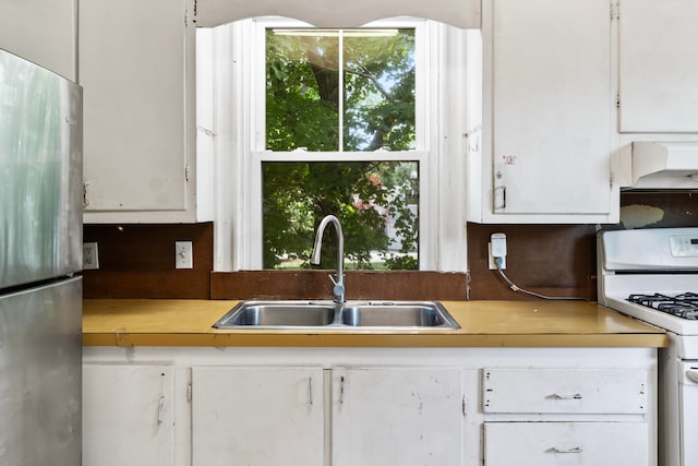 kitchen featuring stainless steel refrigerator, sink, white gas range, and white cabinetry