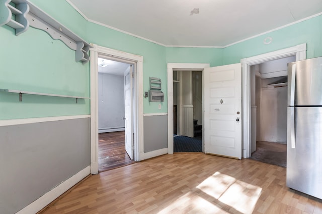 unfurnished bedroom with ornamental molding, light wood-type flooring, a baseboard radiator, and stainless steel refrigerator