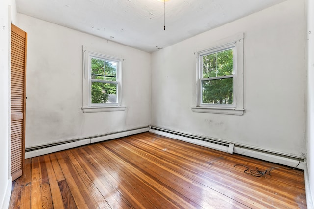 unfurnished room with hardwood / wood-style floors, a baseboard heating unit, and plenty of natural light