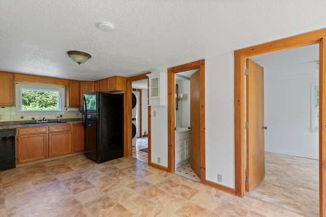 kitchen featuring stacked washing maching and dryer, black appliances, decorative backsplash, and a textured ceiling