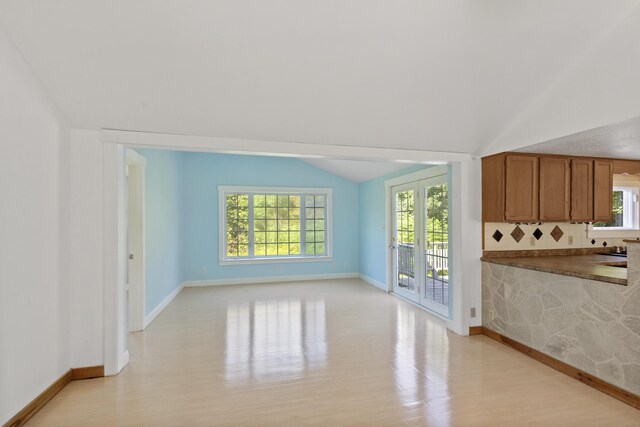 unfurnished living room with light wood-type flooring, vaulted ceiling, and a wealth of natural light