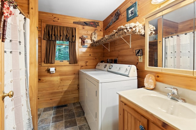 clothes washing area featuring wood walls, dark tile patterned flooring, sink, and washing machine and dryer