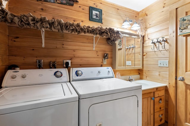 clothes washing area with sink, washing machine and dryer, cabinets, and wooden walls