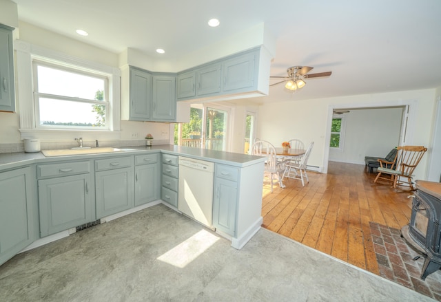 kitchen featuring sink, light wood-type flooring, a wood stove, dishwasher, and ceiling fan