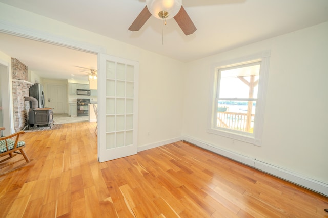 unfurnished room with a wood stove, baseboard heating, and light wood-type flooring